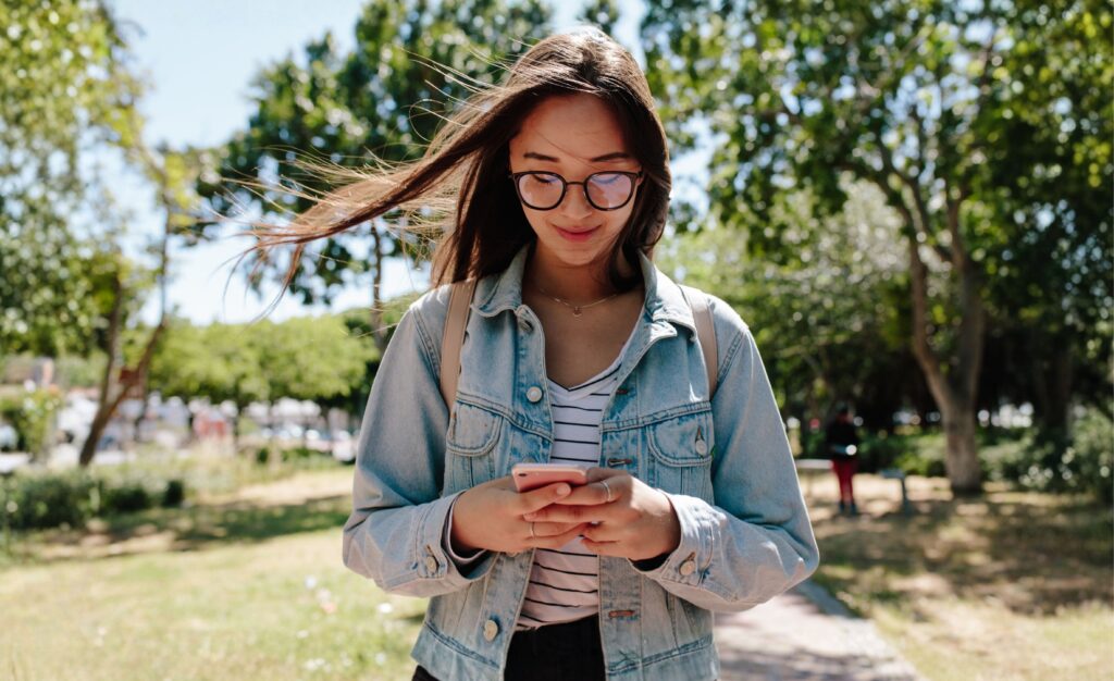 Girl with glasses is looking down at her phone with a slight smile on her face