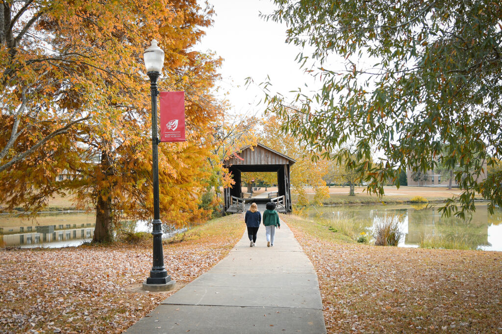 UWA Campus featuring two students walking towards the Covered Bridge in the fall.