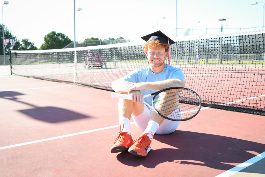 Student athlete, Lucas Hammond poses with graduation cap and tennis racket on the the UWA Tennis Courts
